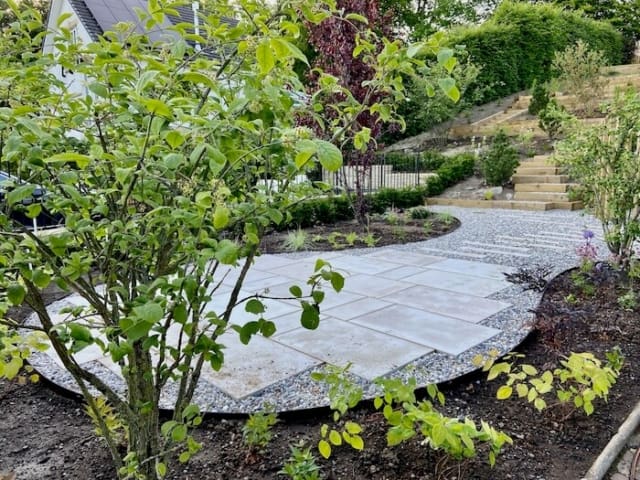 Circular sandstone paved seating area set within planting in this family garden